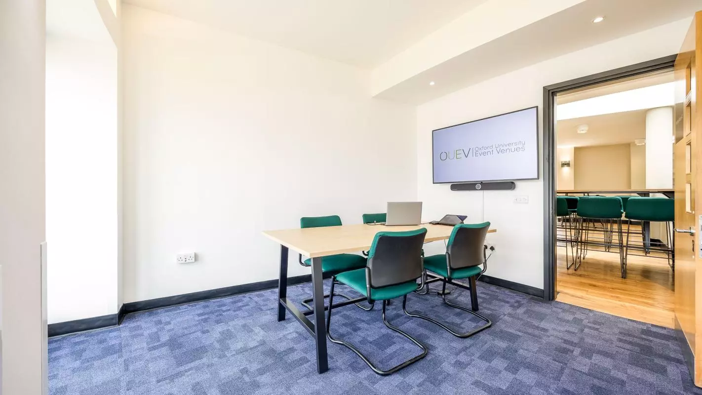 Meeting room with rectangular table and four green chairs placed on the outside