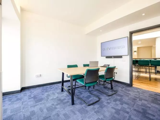 Meeting room with rectangular table and four green chairs placed on the outside